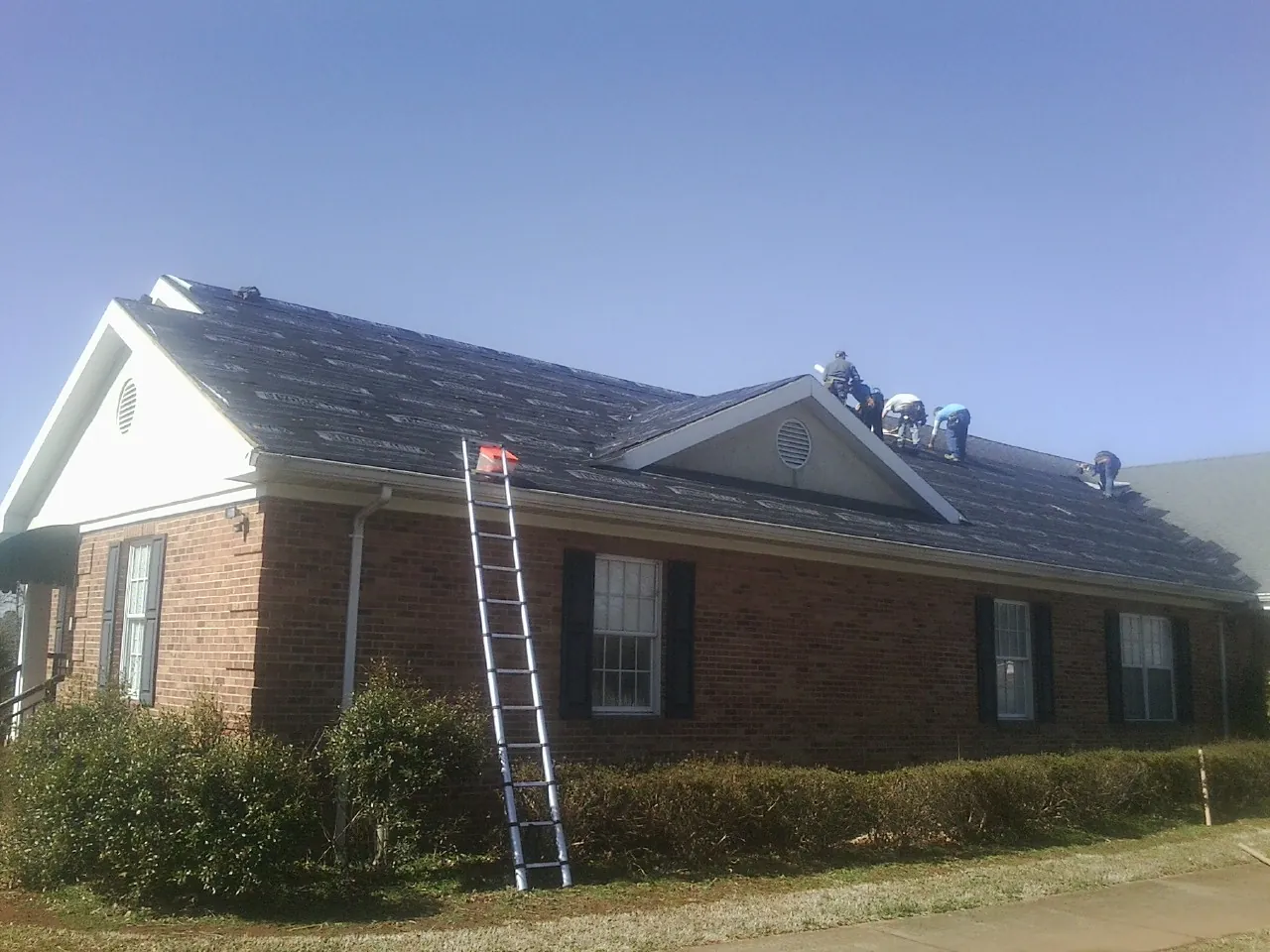 Crew tearing shingles off a brick ranch roof with a ladder set — Metal Roof Repair work by our crew in Lemont