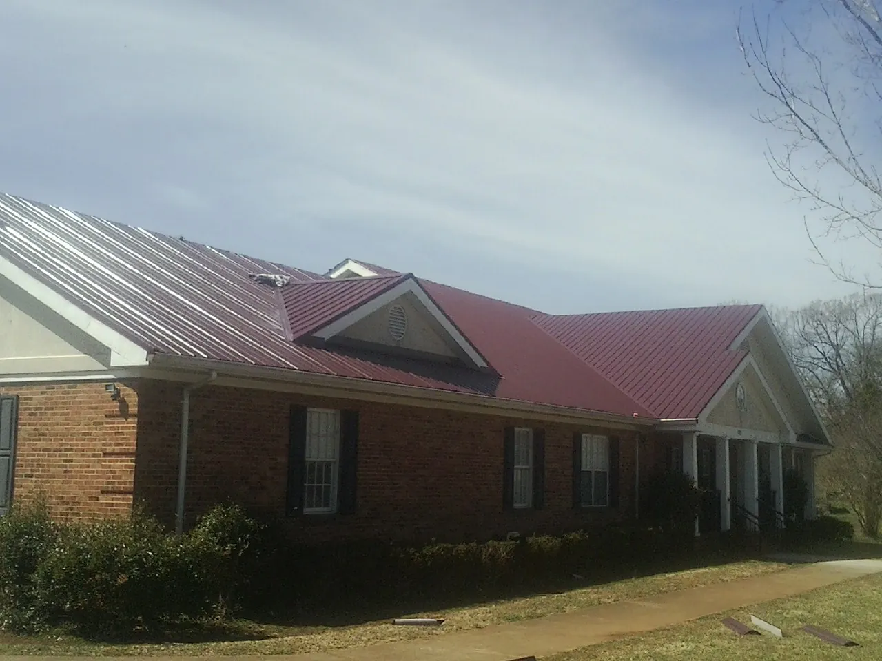 Red metal roof with gabled entries on a long brick building, from a Hail Damage Roof Repair job in Lemont