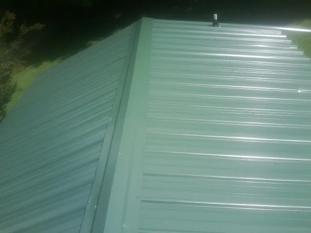 New green metal panels meeting at the ridge of a roof — Flat Roof Repair work by our crew in Lemont