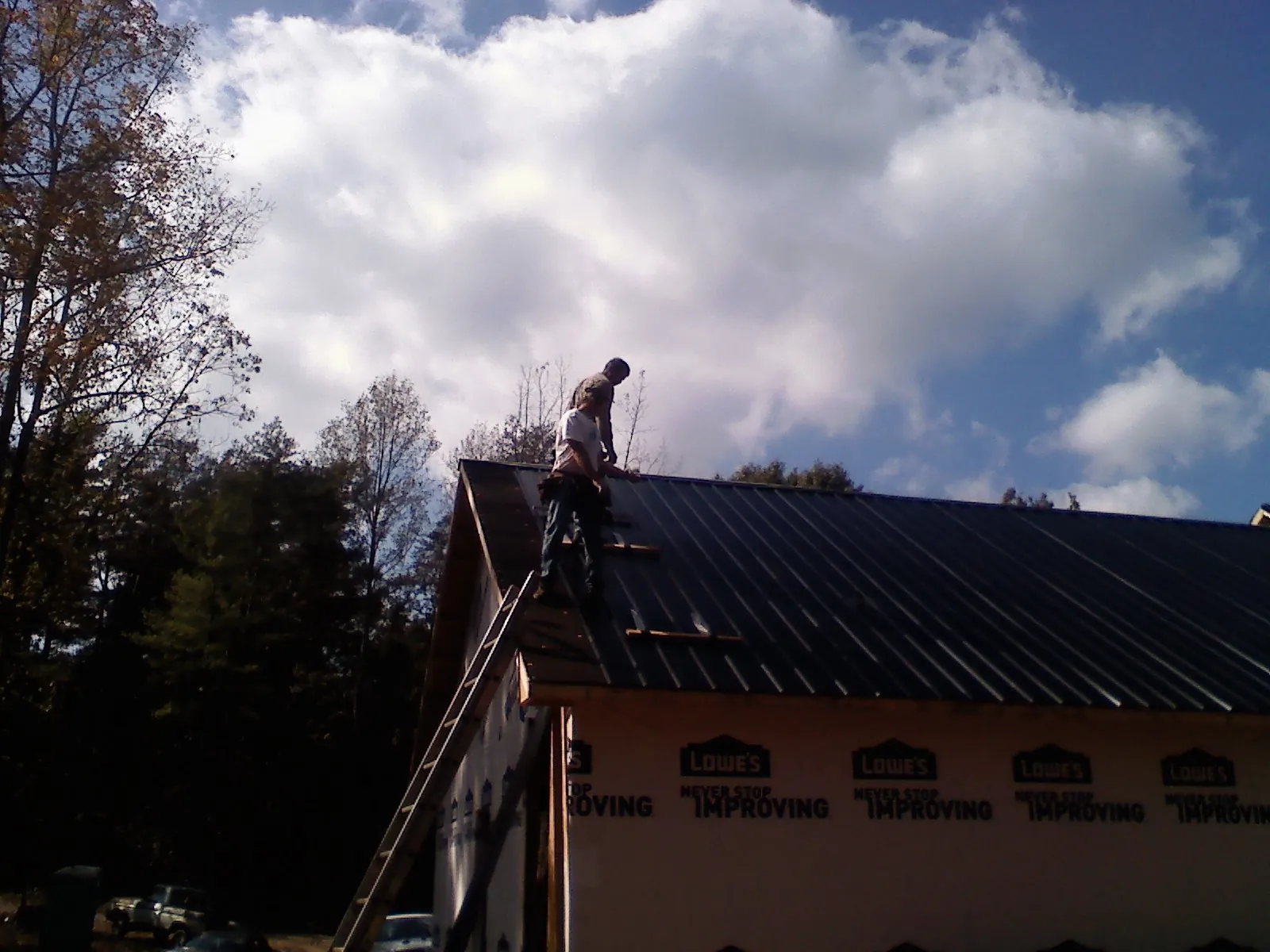Roofer fastening dark metal panels high against a cloudy sky, from a Roof Inspection job in Lemont