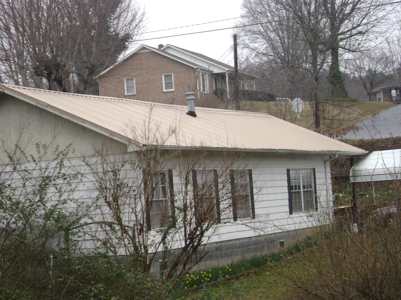 Tan metal roof on a white sided house set into a hillside — Commercial Roofing by Roofing Brothers in Lemont